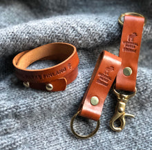 Lataa kuva Galleria-katseluun, Nahkainen avainlenkki kultaisella metalliosalla ja nahkainen rannekoru harmaan villapaidan päällä