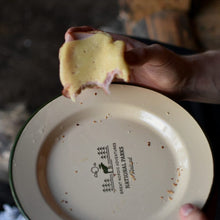 Lataa kuva Galleria-katseluun, Luonnonvalkoinen emalilautanen metsänvihreällä hirvi national park finland painatuksella ja käsi jossa leipä
