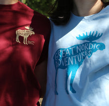 Load image into Gallery viewer, Kaksi tyttöä luonnossa jolla päällä viininpunainen t-paita jossa pieni hirvipainatus ja vaaleansininen t-paita jossa iso hirvipainatus
