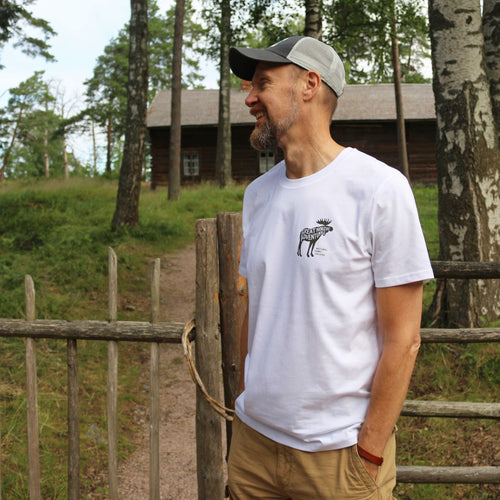 Iloinen mies luonnossa jolla päällä valkoinen t-paita jossa pieni hirvipainatus